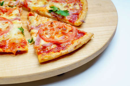 Pizza with slices of sausage, cheese, olives and tomatoes cut into rings. Pizza on a light wooden platter. The background is a light gray canvas, next to a bunch of parsley, peppers, tomatoes.の写真素材