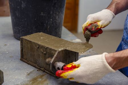 A member of the construction of the laboratory takes a sample of concrete. He loads the concrete into a special mold with a trowel. The result is a cubic concrete blankの写真素材