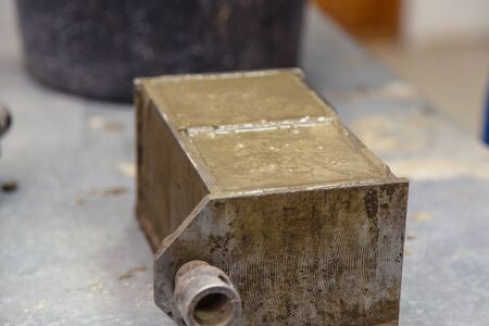 A member of the construction of the laboratory takes a sample of concrete. He loads the concrete into a special mold with a trowel. The result is a cubic concrete blankの写真素材