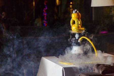 Hookah on oranges and bananas. A hookah bowl consists of two oranges and three bananas strung on top of each other.  The hookah flask is round and transparent, filled with blue-green liquor. Sliced oranges and mint leaves float in the liquor.  Dark bの写真素材