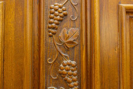 Bunches and leaves of grapes are carved on the wooden front door of the cottage and covered with varnish. Oak front doorの写真素材