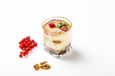Panna cotta dessert in a clear glass. The dessert is decorated with powdered sugar and cranberry berries. A glass on a white background, next to a walnut and a sprig of red currant.の写真素材