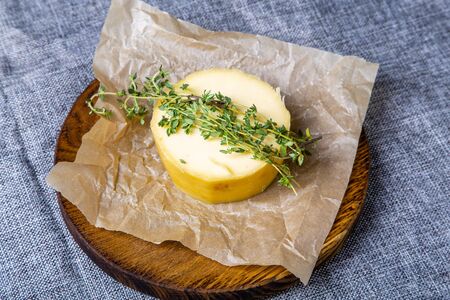 A round head of cheese lies on oiled paper and a wooden tray. Grey canvas background.の写真素材