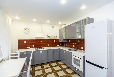 Modern stylish large kitchen in the cottage. Kitchen in red and steel colors. The doors are steel-colored, and the tiles on the wall are red. The floor tiles are beige. White table with four chairsの写真素材