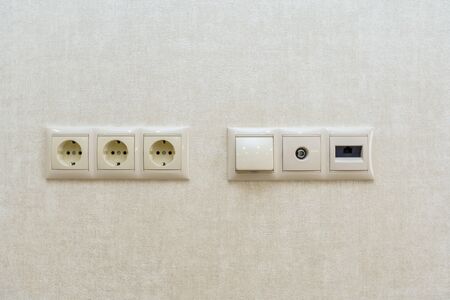 three electrical outlets on the wall against a background of sand colored Wallpaper with a pattern of oval lines.の写真素材