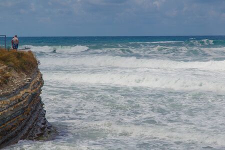 Storm waves upon the rocky promontory, on which are growing pine trees.