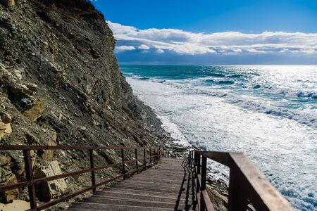 The stairs descend to the shingle beach to the stormy sea On the sea big waves with foam. To the...