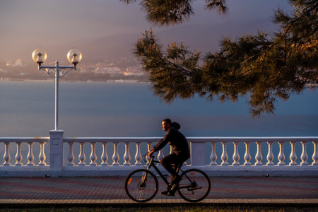 A man rides a Bicycle along the embankment with a balustrade and lanterns. The setting sun is...