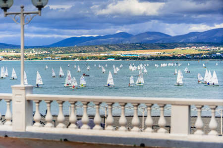 White sails of yachts at sea, youth yacht regatta. In the foreground there is an embankment and a...