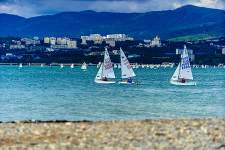 Youth yacht regatta in Gelendzhik Bay. Autumn dark sky, green stormy sea. Mountains and houses in...