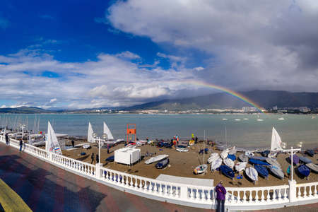 A rainbow over the sea bay where yachts are parked. In the foreground of a yacht on the beach. There are mountains in the background. Storm clouds, sunset. Gelendzhik, Black Seaのeditorial素材