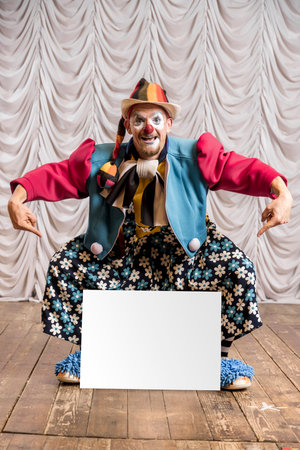 A funny clown shows an empty white sign for the inscription. A clown stands on the stage against the backdrop of the stage scenes.の写真素材