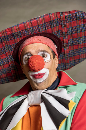 A clown with a red nose and a red hat is smiling. The clown is wearing a green jacket and a red hatの写真素材