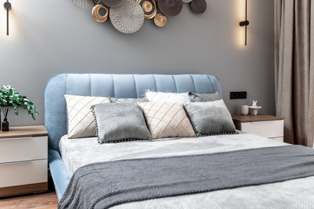 A bed with pillows and a lamp on the nightstand. The bed is blue and the pillows are white and gray