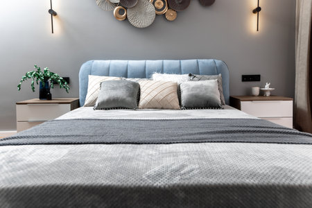A bed with pillows and a lamp on the nightstand. The bed is blue and the pillows are white and gray