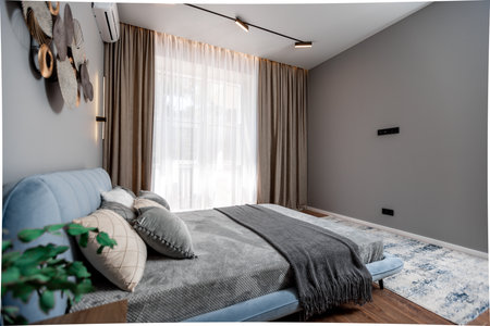 A bedroom with a blue bed and a gray blanket. The room is decorated with a few plants and a potted plantの写真素材