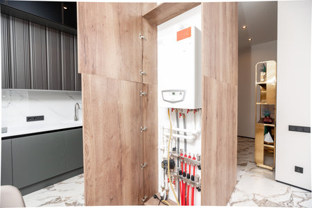 A white and black water heater is in a wooden cabinet. The cabinet is open and the water heater is visibleの写真素材