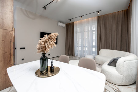 A living room with a white couch, a white chair, and a white coffee table. A vase with flowers on it sits on the tableの写真素材