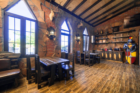 A rustic restaurant with a wooden floor and a large wooden table. The tables are surrounded by chairs and there are several potted plants in the roomの写真素材