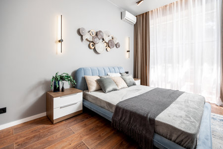 A bedroom with a large bed, a nightstand, and a window. The bed is covered with a gray blanket and...