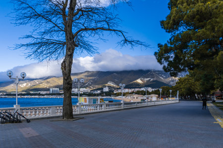 Gelendzhik resort in winter. Nord-Ost wind begins. Signs of storm - clouds over Caucasus Mountains. Off-season. Deserted beach, strong wind. Embankment and balustrade in foregroundの写真素材