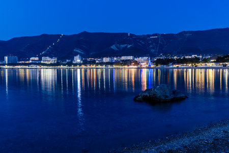 Gelendzhik, Krasnodar Territory, Russia. Gelendzhik resort embankment in the evening, the lamps are rhythmically reflected in Gelendzhik Bay. A beautiful night view of a city with a large body of water in the background.の写真素材