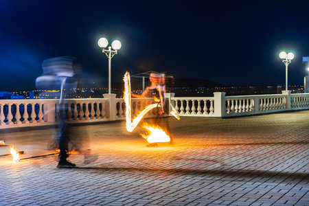 A man is juggling fire on a brick walkway. The fire is orange and the man is wearing a black shirtの写真素材