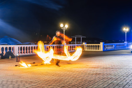 Gelendzhik resort embankment. A man is performing a fire trick on a beach at night. The scene is...