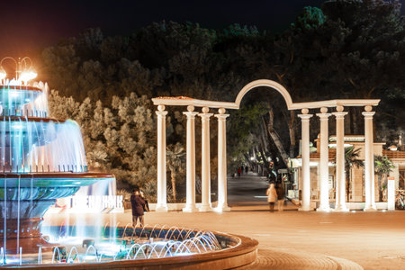 Gelendzhik resort embankment in the evening. The singing fountain. In the background is an arch with columns. The fountain is surrounded by trees and a buildingの写真素材