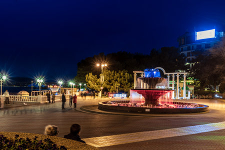 Gelendzhik resort embankment in the evening. There is a musical fountain in the center. Behind it is a colonnade. Balustrade along the sea line. The fountain is surrounded by a green bush. The walkway is lit up at night, creating a peaceful and serene atmosphereの写真素材