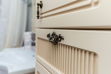 A white cabinet with a gold handle. The cabinet is in a bathroom. The cabinet is made of woodの写真素材