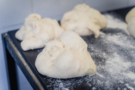 A table with four pieces of dough on it. The dough is covered in flour. The dough is in different...