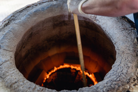 Tandoor, where Uzbek flatbreads are baked on walls. Fire is visible at bottom. The stick is burning...
