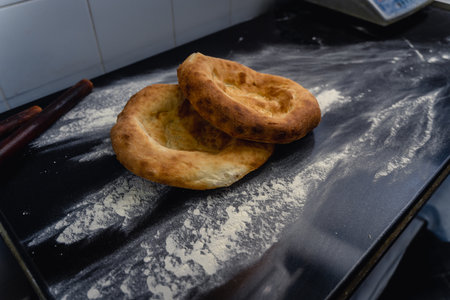Freshly baked appetizing Uzbek flatbreads lie on table sprinkled with flour. On cakes there is...