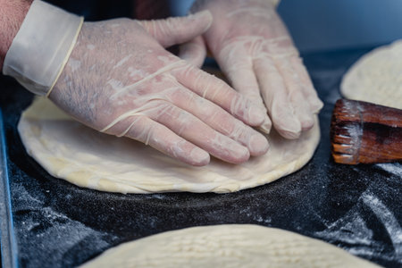 Baker makes Uzbek flatbread from dough. The dough is in the middle of the counter and the person is...