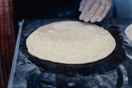 Baker makes pattern on blank for Uzbek flatbread. The dough is covered in flour and the person is wearing glovesの写真素材