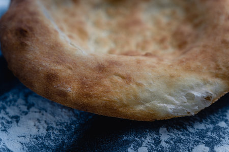 Freshly baked appetizing Uzbek flatbreads lie on table sprinkled with flour. On cakes there is appetizing ruddy crustの写真素材