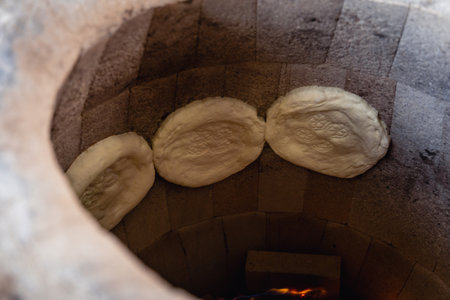 Uzbek flatbreads are baked in tandoor. They hang on the wall of tandoor and begin to brown. Fire is baking from below.の写真素材