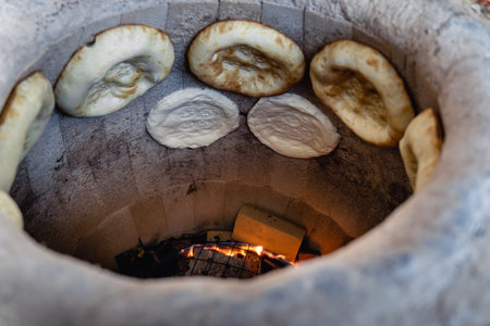 Uzbek flatbread on hay of tandoor and get ready. Fire is burning below. Cakes are ruddy and juicy, with appetizing crust. Flatbreads are cooked right on wall of tandoorの写真素材