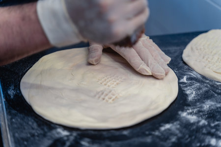 Baker makes pattern on blank for Uzbek flatbread. The dough is covered in flour and the person is...