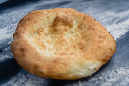 Freshly baked appetizing Uzbek flatbreads lie on table sprinkled with flour. On cakes there is...