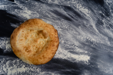 Freshly baked appetizing Uzbek flatbreads lie on table sprinkled with flour. There is appetizing...