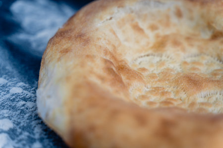 Freshly baked appetizing Uzbek flatbreads lie on table sprinkled with flour. On cakes there is...