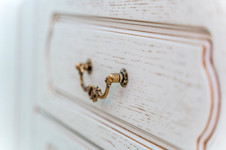 A white dresser with a gold knob on the front. The knob is ornate and has a flower design