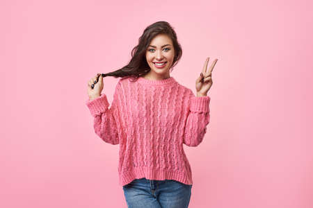 Portrait of a happy cheerful girl showing peace gesture with hand. Isolated over a pink background. Victory symbol.の写真素材