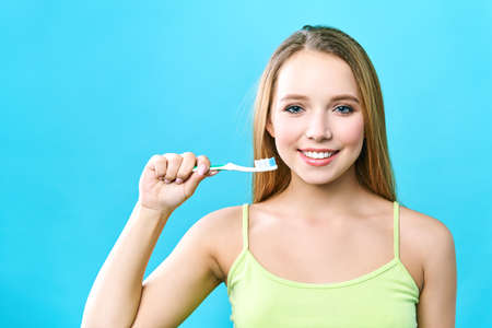 portrait of attractive caucasian smiling woman isolated on blue studio shot brushing her teeth