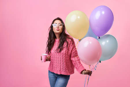 Happy young smiling woman with balloons in her hand, on a pink background