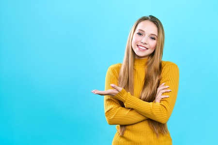 Portrait cheerful pretty young lady standing isolated over blue background. Looking camera showing...