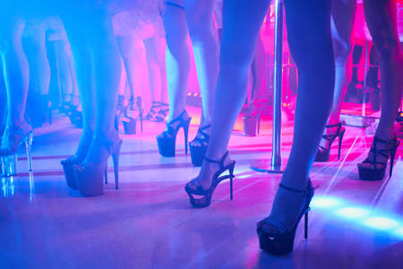 Young sexy woman pole dancing striptease with pylon in night club. Beautiful naked stripper girl on stage. Beautiful female legs in high-heeled shoes stripsの写真素材