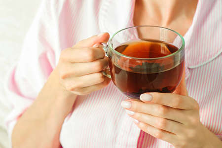 Young woman relaxing on sofa holding cup with lemon tea. Woman dreaming in living room lying on couch. Woman thinking while drinking lemon tea at home.の写真素材